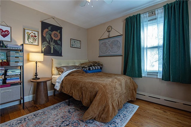 bedroom with a baseboard radiator, wood finished floors, ceiling fan, and multiple windows