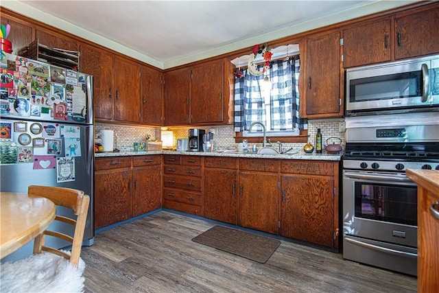 kitchen featuring appliances with stainless steel finishes, dark wood-style floors, brown cabinets, decorative backsplash, and a sink