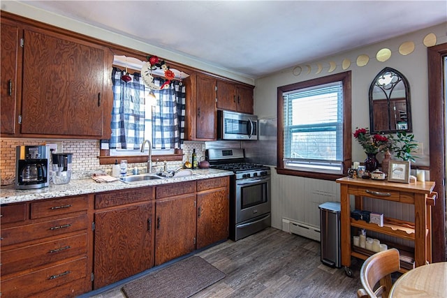 kitchen featuring appliances with stainless steel finishes, baseboard heating, a wainscoted wall, dark wood finished floors, and a sink