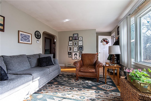 living room featuring a baseboard radiator, a healthy amount of sunlight, wood finished floors, and arched walkways