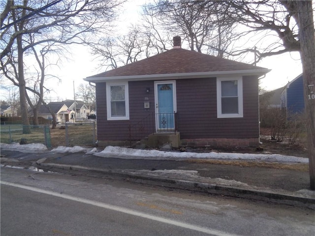 bungalow-style home with roof with shingles, fence, and a chimney