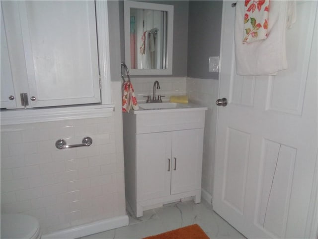 bathroom with tile walls, marble finish floor, toilet, vanity, and wainscoting