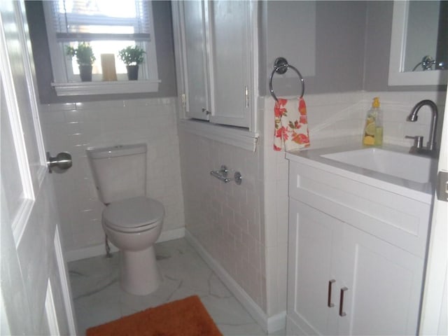 bathroom with marble finish floor, vanity, toilet, and wainscoting