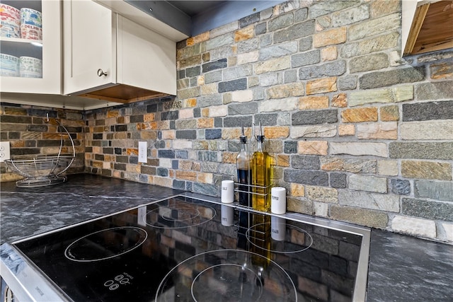 kitchen with dark countertops, tasteful backsplash, glass insert cabinets, white cabinetry, and stovetop