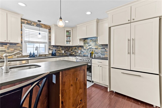 kitchen with paneled built in fridge, a sink, dark countertops, and pendant lighting