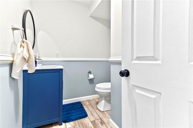 half bath with toilet, wood finished floors, baseboards, and vanity
