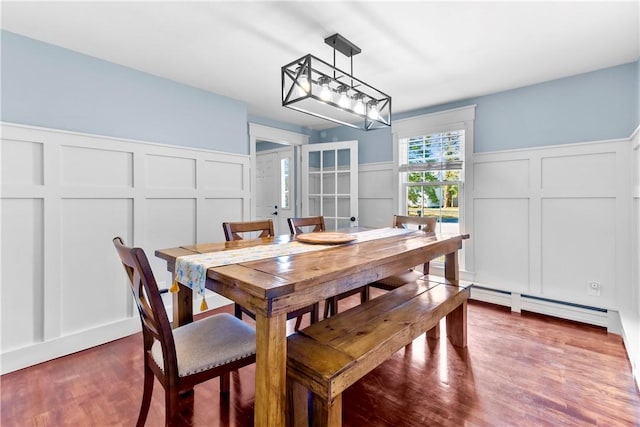 dining area featuring a wainscoted wall, french doors, wood finished floors, a baseboard radiator, and a decorative wall