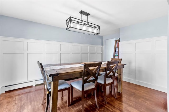 dining space featuring a baseboard radiator, a decorative wall, a wainscoted wall, and wood finished floors