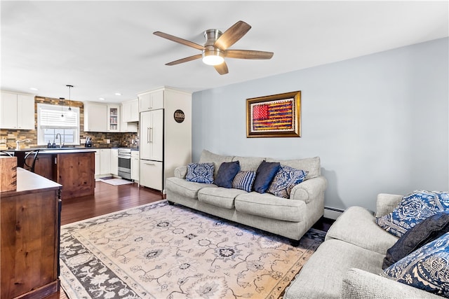 living area with dark wood finished floors, baseboard heating, and ceiling fan