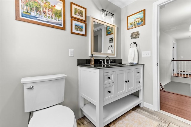 half bath featuring a baseboard radiator, wood finished floors, toilet, and vanity
