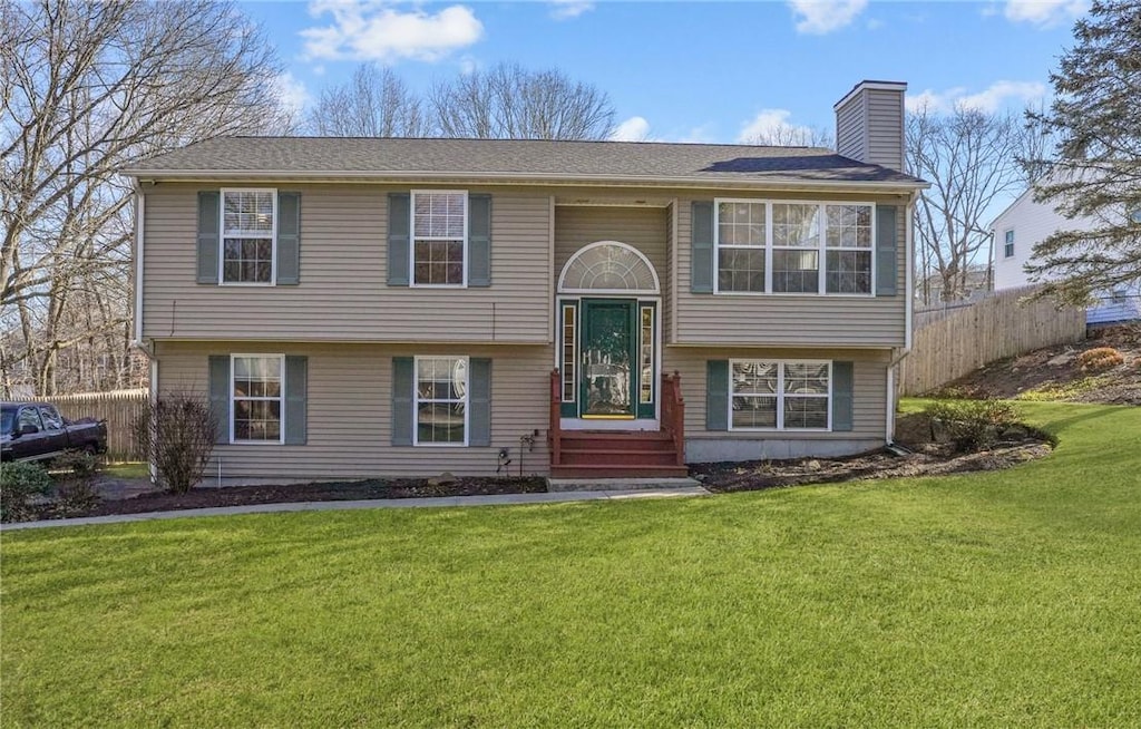 split foyer home featuring a front lawn, fence, and a chimney