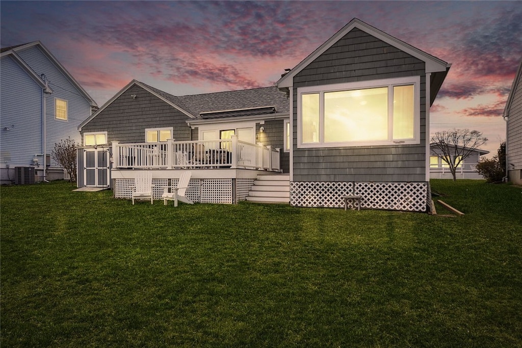 back of property at dusk with cooling unit, a wooden deck, and a lawn