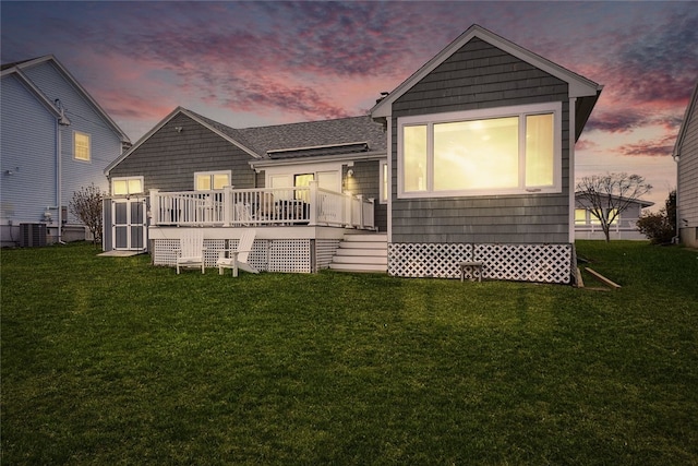 back of property at dusk with cooling unit, a wooden deck, and a lawn