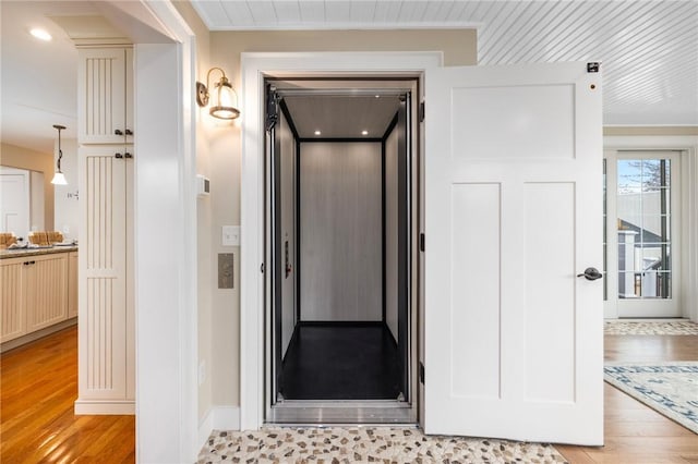 hall featuring elevator, crown molding, and light wood-style floors