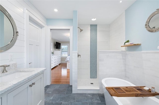 full bathroom with connected bathroom, a tile shower, vanity, a freestanding bath, and tile walls