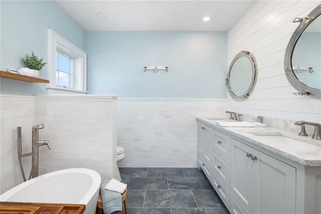 full bathroom with double vanity, wainscoting, a freestanding bath, and a sink