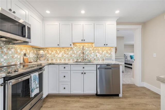 kitchen featuring white cabinetry, tasteful backsplash, light wood-type flooring, stainless steel appliances, and a sink