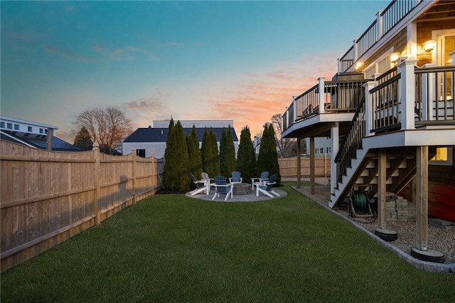 yard at dusk featuring a patio, stairs, a fenced backyard, a deck, and a fire pit