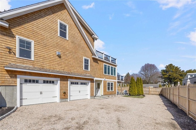 back of property with gravel driveway, fence, and a garage