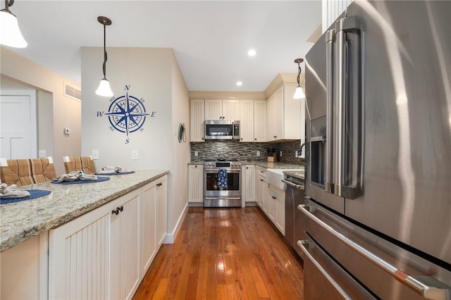 kitchen featuring light stone countertops, wood-type flooring, stainless steel appliances, visible vents, and decorative backsplash
