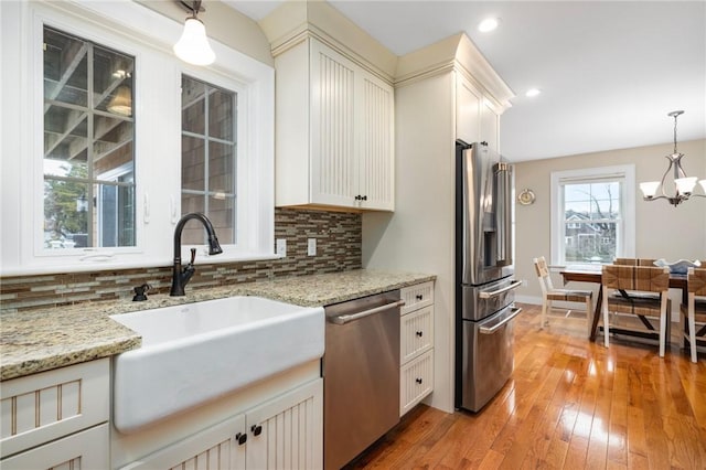 kitchen with light wood finished floors, stainless steel appliances, a sink, hanging light fixtures, and backsplash