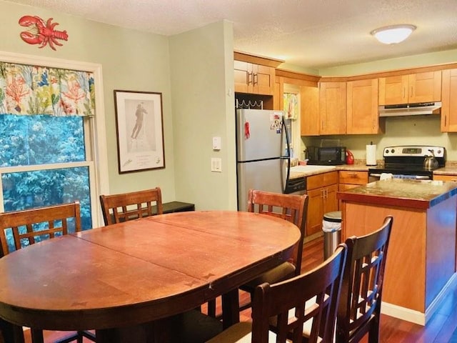 kitchen featuring a kitchen island, dark wood-style floors, a textured ceiling, under cabinet range hood, and stainless steel appliances