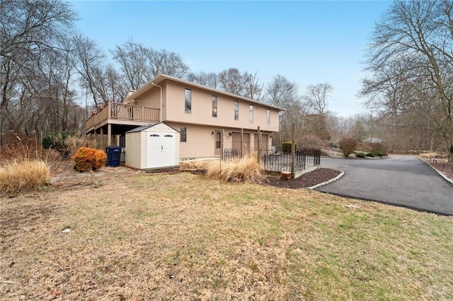 rear view of house featuring aphalt driveway, an outdoor structure, a lawn, and a storage unit