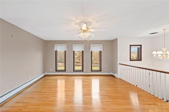 spare room featuring ceiling fan with notable chandelier, light wood-style flooring, visible vents, a baseboard heating unit, and baseboards