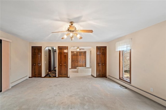 unfurnished bedroom with baseboard heating, arched walkways, connected bathroom, and carpet floors