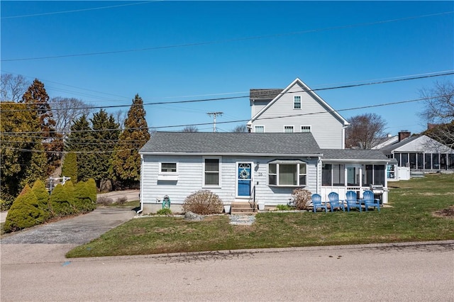 view of front of home featuring a front lawn, a shingled roof, a sunroom, and entry steps