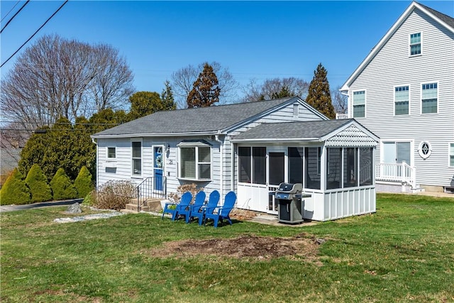 back of house with roof with shingles, a sunroom, and a yard