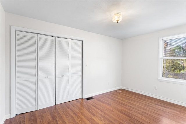 unfurnished bedroom featuring baseboards, a closet, wood finished floors, and visible vents