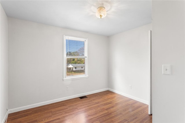 empty room featuring baseboards, wood finished floors, and visible vents