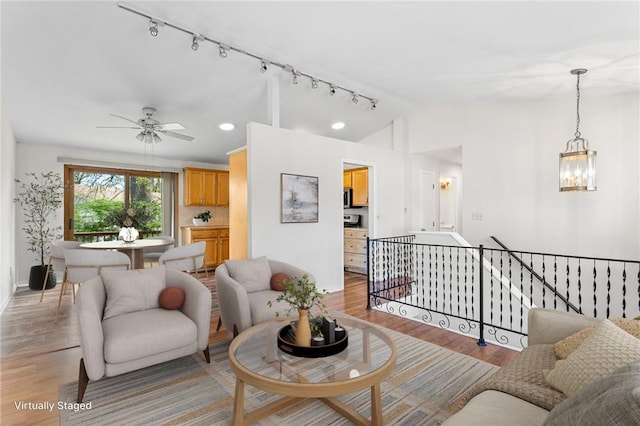living area featuring ceiling fan with notable chandelier, baseboards, vaulted ceiling, and light wood-type flooring