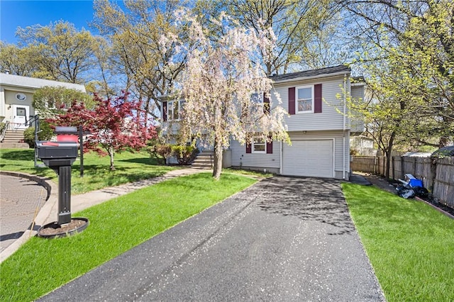 raised ranch with an attached garage, aphalt driveway, fence, and a front yard