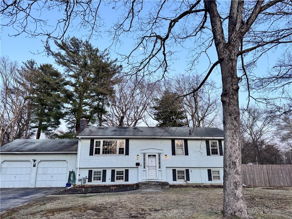 raised ranch featuring a chimney, an attached garage, fence, and aphalt driveway