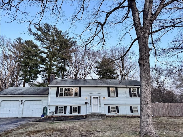 raised ranch featuring a chimney, an attached garage, fence, and aphalt driveway