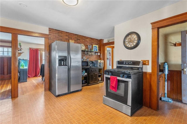 kitchen with wood walls, stainless steel appliances, brick patterned floor, and wainscoting