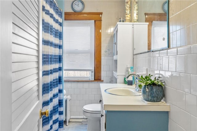 bathroom with radiator heating unit, vanity, a wealth of natural light, and tile walls