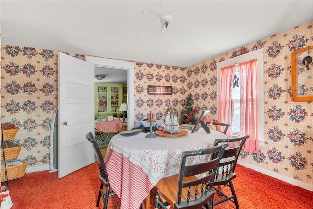 dining room featuring baseboards, wallpapered walls, and light carpet