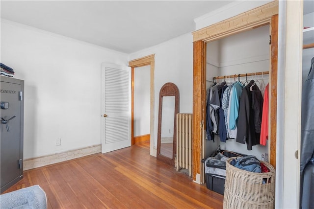 bedroom featuring radiator, baseboards, a closet, ornamental molding, and wood finished floors