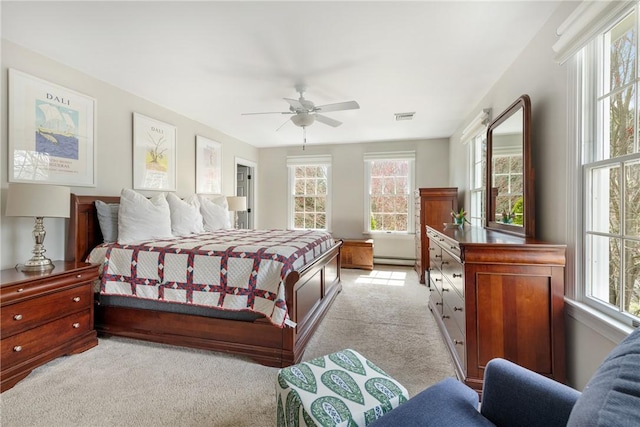 bedroom featuring a baseboard heating unit, visible vents, light colored carpet, and ceiling fan