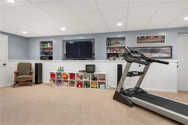 workout room featuring carpet flooring, a paneled ceiling, a wainscoted wall, and built in shelves