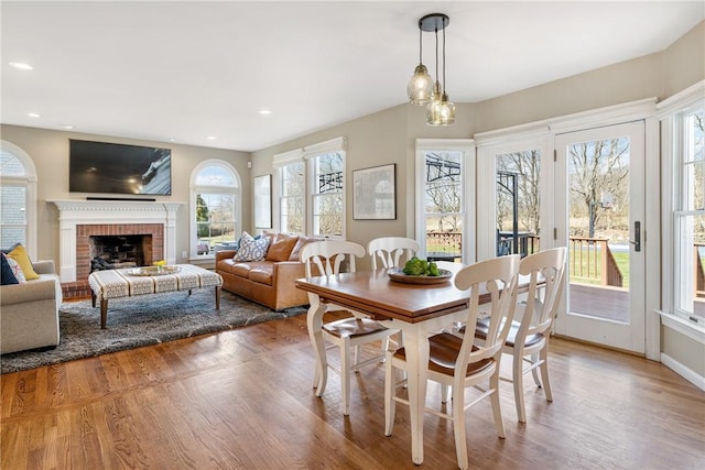 dining space featuring wood finished floors, a brick fireplace, plenty of natural light, and recessed lighting