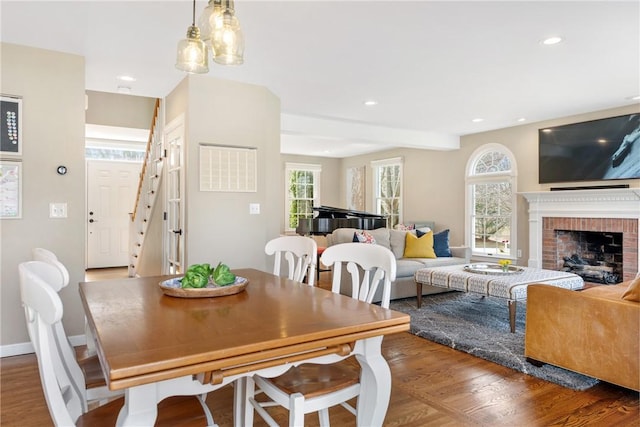 dining space with wood finished floors, stairs, a brick fireplace, and recessed lighting