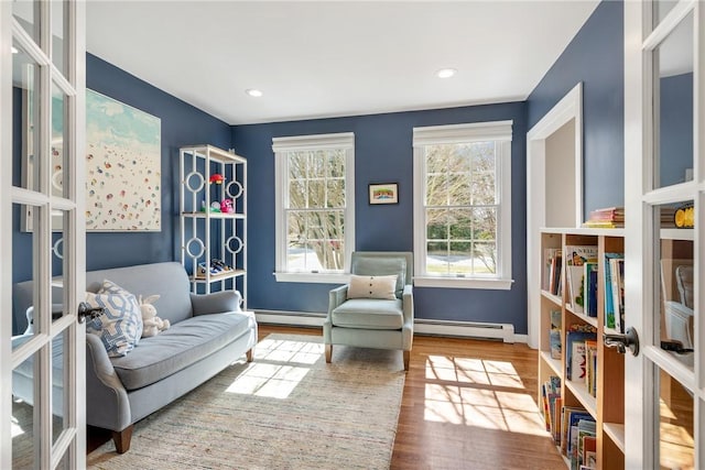 living area featuring baseboards, baseboard heating, wood finished floors, french doors, and a baseboard heating unit
