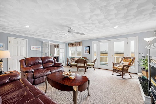 living room with a ceiling fan, crown molding, french doors, a fireplace, and light colored carpet