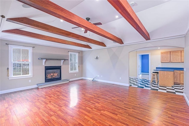 unfurnished living room featuring lofted ceiling with beams, baseboards, light wood-style flooring, and a glass covered fireplace
