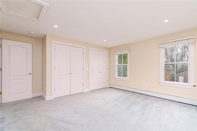 unfurnished bedroom featuring baseboard heating, two closets, carpet, baseboards, and recessed lighting