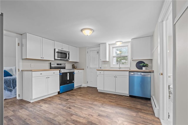 kitchen featuring stainless steel appliances, white cabinets, a baseboard radiator, and wood finished floors